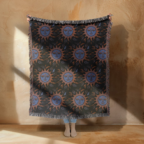 Luxurious woven cotton throw blanket featuring mystical blue sun faces with copper rays on black background, bordered by elegant fringe. Perfect celestial wall hanging, witchy bedroom decor, or dark academia throw for couch or bed.